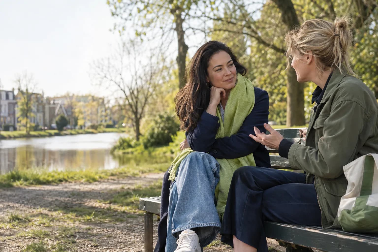 Twee vrouwen praten op een bankje aan het water; de een luistert aandachtig