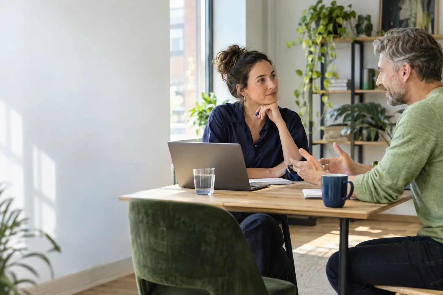 Twee collega's zitten tegenover elkaar aan een kleine tafel op kantoor in een rustig gesprek